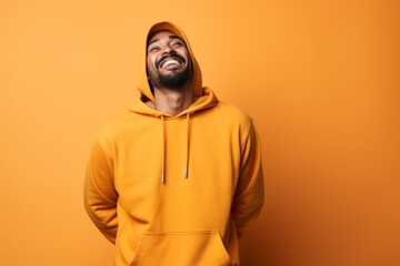 Poster - Portrait of a grinning indian man in his 20s sporting a comfortable hoodie while standing against soft orange background