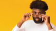 © Prostock-studio - Handsome african american man adjusting his lasses and looking at camera, orange studio background, close up