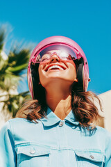 Wall Mural - A woman wearing a pink helmet is smiling and looking up at the sky