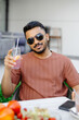 © nazariykarkhut - Handsome man sitting outside at a restaurant table and drinking iced beverage in cafe