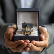 © AlirezA - A man presents a miniature house inside a jewelry box, symbolizing a real estate gift, in an elegant indoor setting