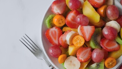 Wall Mural - Top view of of summer fresh fruit salad in a bowl. Healthy food for breakfast. Mixed strawberries, grapes, banana, kiwi, peach, kumquat for diet lunch