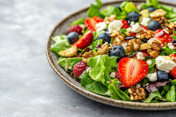 A fresh salad featuring mixed greens, strawberries, blueberries, walnuts, and feta cheese served on a rustic plate,