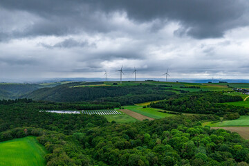 Wind farm and solar panel station amidst green forest. Overcast rainy skies. Green energy extraction concept.