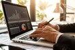 © Tasnim - Businessman working on a laptop with financial charts and graphs on screen. Office workspace with data analysis.