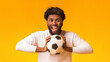 © Prostock-studio - Excited african american football fan with ball on orange background, copy space