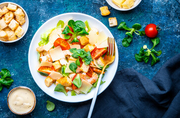 Caesar salad with shrimp, tomatoes, iceberg lettuce, croutons, parmesan cheese and classic dressing. Blue background, top view