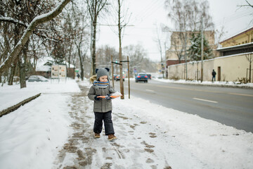 Wall Mural - Adorable little boy having fun in a city on snowy winter day. Cute child wearing warm clothes playing in a snow.