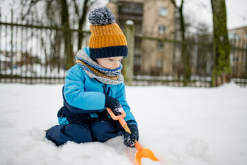 Wall Mural - Adorable little boy having fun on snowy winter day. Cute child wearing warm clothes playing in a snow.