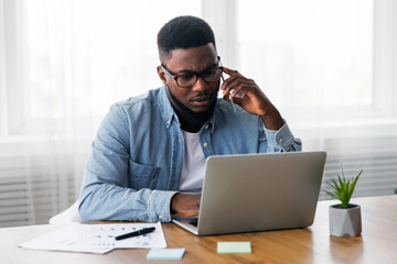 concerned african american employee talking on mobile phone and looking at laptop screen, having iss