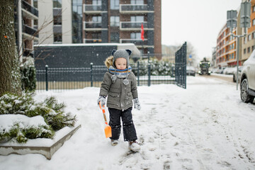 Wall Mural - Adorable little boy having fun in a city on snowy winter day. Cute child wearing warm clothes playing in a snow.