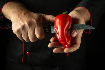 Canvas Print - Cutting red bell pepper with knife in hands of cook. Low key concept of cooking vegetable breakfast. Chop the pepper