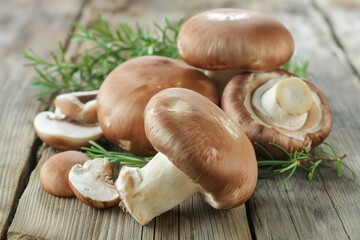 Poster - A bunch of mushrooms are on a wooden table. The mushrooms are of different sizes and some are cut open. The mushrooms are surrounded by green herbs, giving the image a fresh and natural feel