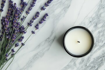 There is a relaxing spa concept behind the lavender arrangement and the aromatic candle in a jar displayed on a white marble table. There is a top view, flat lay, and copy space all relating to the