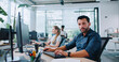 © ihorvsn - Gorgeous Caucasian man in shirt working in business company looking to camera. Busy specialist looking directly at screen and using keyboard to type message. In background people sitting at computers.