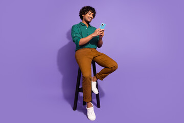 Full body length photo of handsome mexican guy sitting stool with smartphone waiting for girlfriend isolated on violet color background