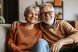 © Digital Storm - Portrait of attractive aged retired couple hugging resting together at home sit on sofa laughing looking at camera, enjoy their relationships lifelong marriage and carefree life on retirement