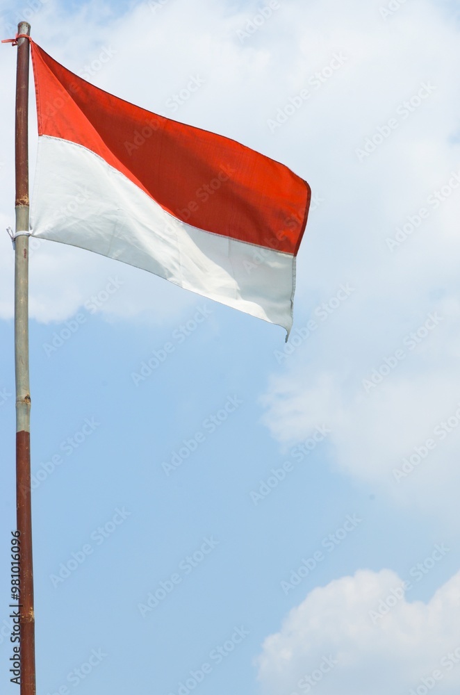 The red and white Indonesian flag on a bamboo pole flutters in the wind ...