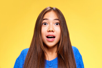 Wall Mural - Close portrait of young attractive little girl, gazes at distance with widely open eyes, in shock against bright yellow studio background. Seles season begin. Concept of human emotions, expression. Ad