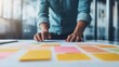 © ArtifyGraphy - A businessman in a casual shirt organizing project ideas on a desk covered with colorful sticky notes, planning strategy and goals.