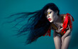 © Connect Images - Woman with long flowing black hair and striking yellow eye makeup wearing a red harness on a teal background.