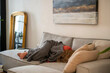 © Connect Images - Person relaxing on a gray couch covered with a gray blanket in a cozy living room with modern decor.
