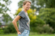 © Connect Images - Confident woman standing in a park with her hand on her hip, smiling at the camera.