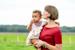 © Connect Images - Mother affectionately kissing her baby who looks pensive against a rural backdrop.
