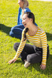 © wavebreak3 - Sitting on grass, young woman laughing with diverse friends outdoors, enjoying sunny day