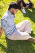 © wavebreak3 - Sitting on grass, young man enjoying sunny day with diverse friends outdoors
