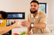© wavebreak3 - Smiling man in kitchen handing cup to friend while preparing vegetables