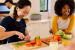 © wavebreak3 - Chopping vegetables, woman smiling while preparing meal with diverse friends in kitchen
