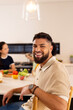 © wavebreak3 - Smiling man sitting at kitchen counter with diverse friends preparing food in background, copy space