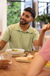 © wavebreak3 - Smiling man enjoying meal with diverse friends, sitting at dining table, socializing