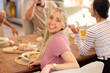 © wavebreak3 - Smiling young woman sitting at dining table with diverse friends, enjoying meal together