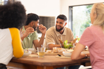 Friends enjoying meal together, laughing and chatting around dining table