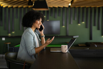 Talking on smartphone, woman working on laptop in modern office space