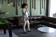 © wavebreak3 - Talking on smartphone, woman standing in modern office with laptop on couch