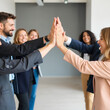 © Ideal & Ideas - A group of colleagues in casual business attire, giving a high five together, symbolizing teamwork, unity, and success.