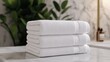 © Natawut - A stack of neatly folded white towels on a countertop, with green foliage and a soft background enhancing the serene and clean atmosphere.