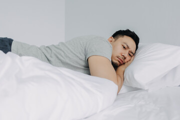 Serious and depressed asian man overthinking the problems lying on the bed.