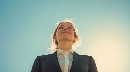 A businesswoman stands confidently in a tailored suit outdoors under a bright blue sky, looking upward with a smile that exudes success and determination