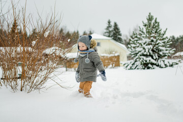 Wall Mural - Adorable little boy having fun on snowy winter day. Cute child wearing warm clothes playing in a snow.