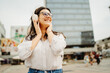 © Dusan - Young caucasian woman listening to music or audio book in the city