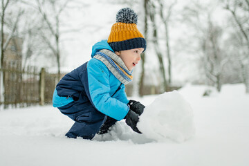 Wall Mural - Adorable little boy having fun on snowy winter day. Cute child wearing warm clothes playing in a snow.