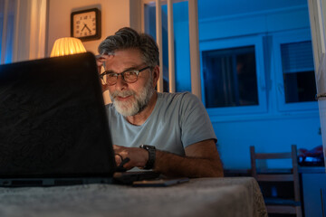 Wall Mural - one man adult caucasian work on laptop at home happy smile. senior man sitting at desk with laptop computer at home office, looking and smiling at screen