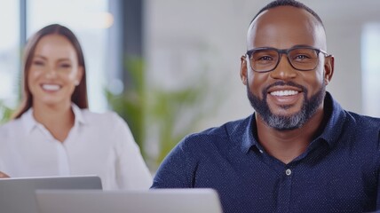 Poster - A man with glasses is smiling and sitting in front of a laptop