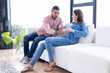 © Wavebreak Media - At home, Expecting multiracial couple sitting on couch, man touching woman's pregnant belly lovingly
