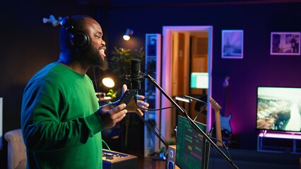Fototapete - Singer performing his new track creation on a microphone, manipulates his audio files recordings with mixing and mastering techniques. Artist composer operates on stereo equipment. Camera B.