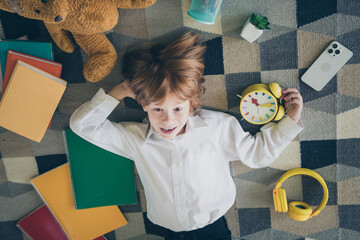 Poster - Photo of charming adorable funny cheerful small boy lying on floor carpet school supply around his cozy house daylight indoors